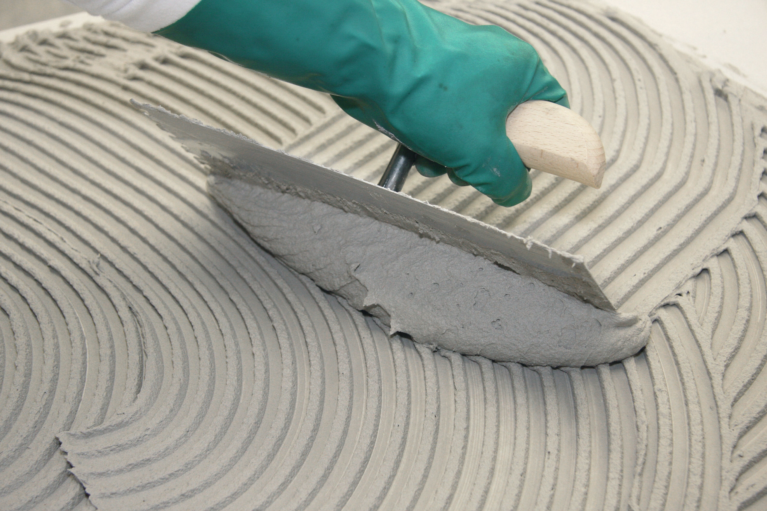 Nahaufnahme einer Maurerkelle beim Aufziehen eines Kammbetts für Fliesenverlegung